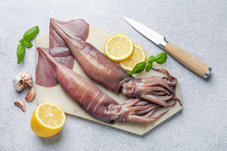 Raw squids, lemon, knife, garlic and basil on light gray table, flat layの写真素材