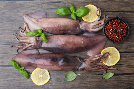 Raw squids, lemon slices, spices and basil on wooden table, flat layの写真素材