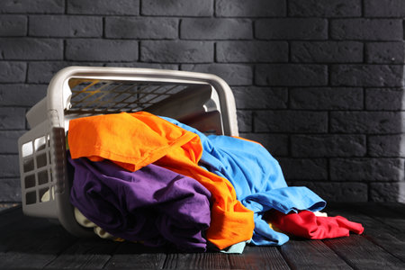 Overturned laundry basket with clothes on black wooden surface. Space for textの写真素材