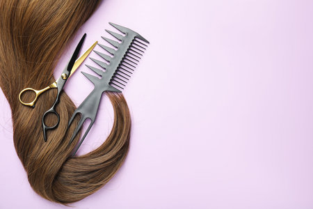 Beautiful brown hair, scissors and comb on light violet background, top view. Space for text