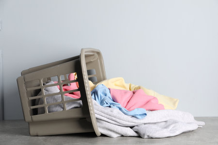 Overturned laundry basket with clothes on gray table against light background. Space for textの写真素材