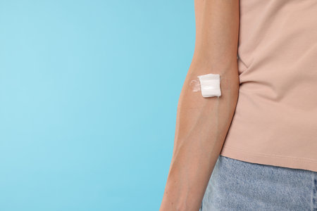Blood donation. Woman with bandage on arm against light blue background, closeup. Space for textの写真素材