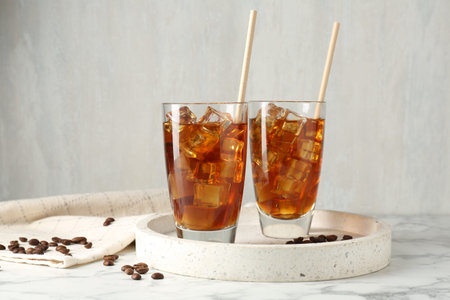 Tasty iced coffee and beans on white marble table