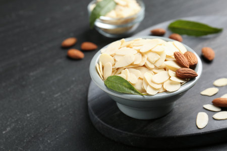 Fresh almond flakes, whole nuts and green leaf in bowl on gray table, closeup. Space for textの写真素材
