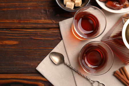 Tasty Turkish tea in glass cups, teapot, brown sugar, dates and cinnamon on wooden table, flat lay. Space for textの写真素材