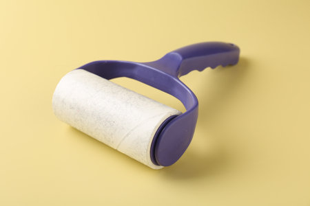 Lint roller with used sticky tape on yellow background, closeup. Space for textの写真素材