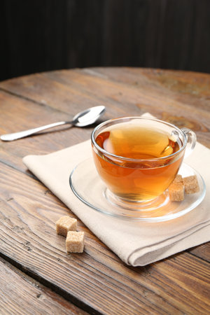 Aromatic black tea in glass cup and brown sugar on wooden table, closeupの写真素材
