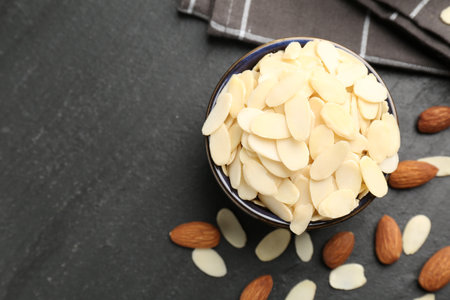 Fresh almond flakes in bowl and whole nuts on gray table, flat lay. Space for textの写真素材