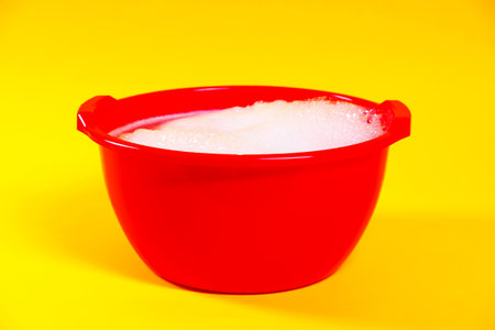 Red plastic basin with soapy water on yellow background, closeupの写真素材