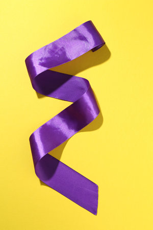 Beautiful violet ribbon on yellow background, top viewの写真素材
