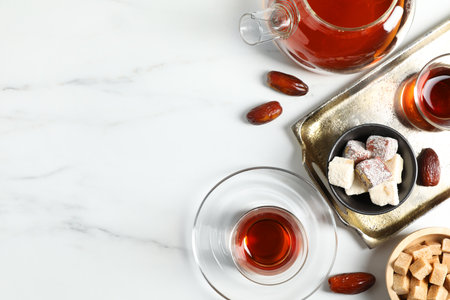Tasty Turkish tea in glass cup, brown sugar, sweets and teapot on white marble table, flat lay. Space for textの写真素材