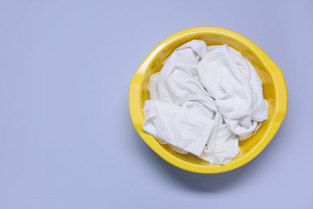 Plastic basin with clothes on light purple background, top view. Space for textの写真素材