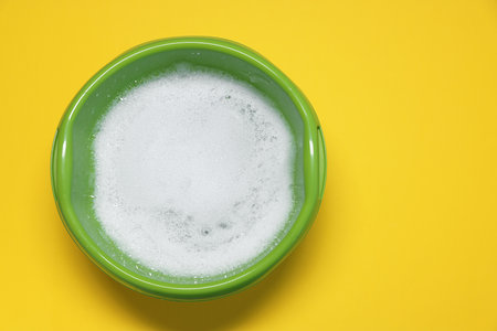 Green plastic basin with water and foam on yellow background, top view. Space for textの写真素材