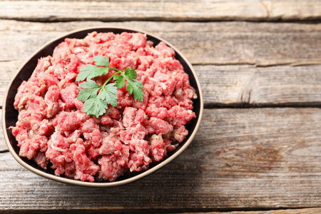 Fresh raw minced meat with parsley in bowl on wooden table, closeup. Space for textの写真素材