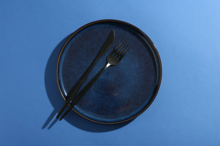Ceramic plate and cutlery on blue background, top viewの写真素材