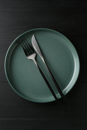 Clean ceramic plate and cutlery on black wooden table, top viewの写真素材