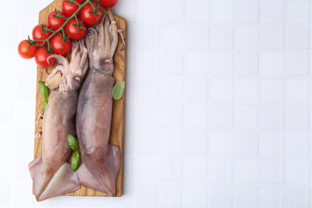 Fresh raw squids, tomatoes and spices on white tiled table, top view. Space for text