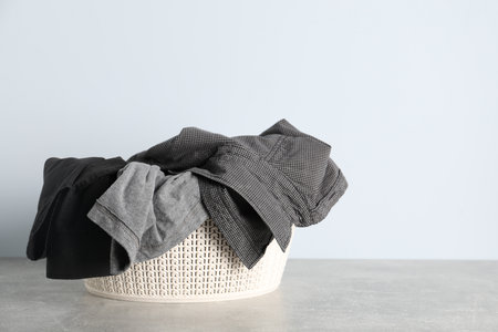 Laundry basket with clothes on gray table against light background. Space for textの写真素材