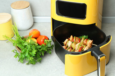 Tasty skewers with chicken and vegetables in air fryer on light gray tableの写真素材