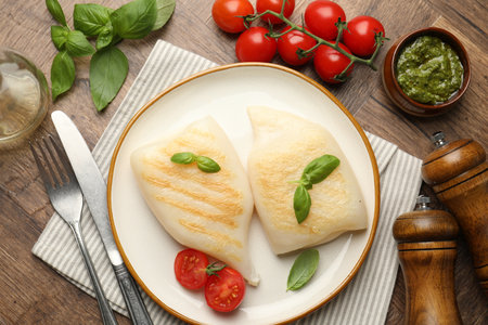 Pieces of tasty grilled squid, tomatoes, basil and sauce served on wooden table, flat layの写真素材