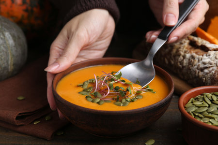 Woman eating delicious pumpkin soup at wooden table, closeupの写真素材