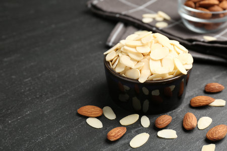 Fresh almond flakes in bowl and whole nuts on gray table, closeup. Space for textの写真素材