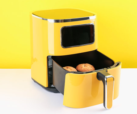 Air fryer with baked muffins on white table against yellow background, closeupの写真素材