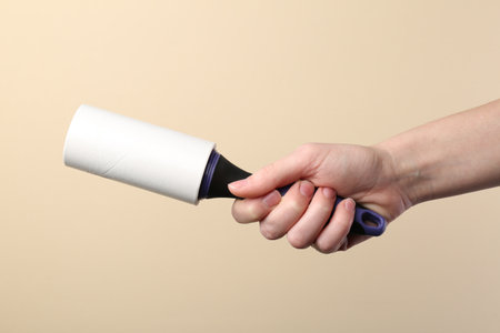 Woman with lint roller on beige background, closeupの写真素材