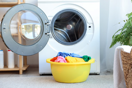 Plastic basin with laundry near washing machine in bathroomの写真素材