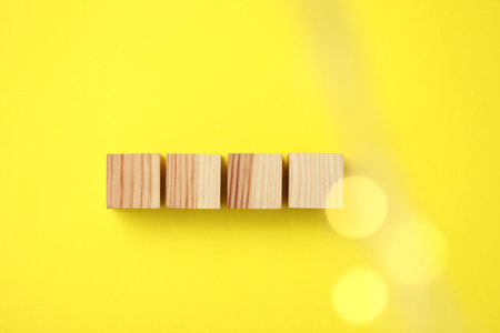 Blank wooden cubes on yellow background, flat lay. Bokeh effect