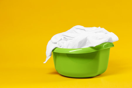 Plastic basin with laundry on yellow background. Space for textの写真素材