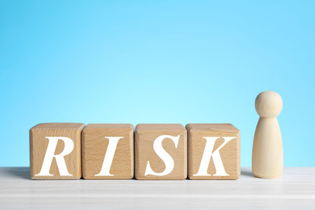 Risk word make of wooden cubes and human figure on white table against light blue background