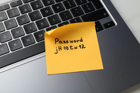 Paper note with password and laptop on white table, above view