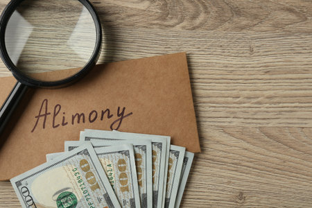 Envelope with word Alimony, money and magnifying glass on wooden table, flat lay. Space for textの写真素材