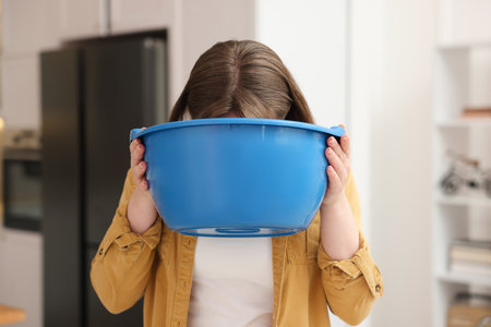 Woman with basin suffering from nausea at homeの写真素材
