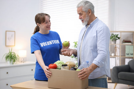 Humanitarian aid for elderly people. Volunteer and senior man with different food products at table...