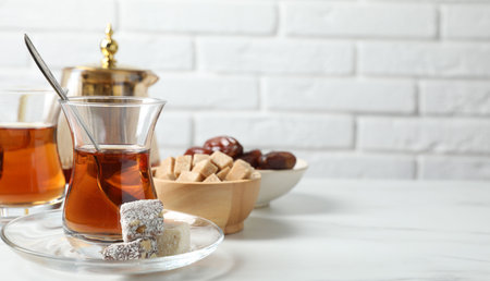 Tasty Turkish tea in glass cups, brown sugar and sweets on white marble table against brick wall, closeup. Space for textの写真素材