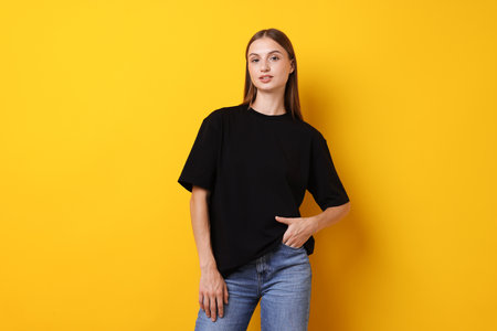 Woman wearing stylish black t-shirt on yellow background. Mockup for designの写真素材