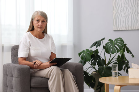 Professional psychotherapist with clipboard in armchair indoorsの写真素材