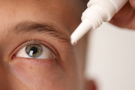 Man applying eye drops on light background, closeup
