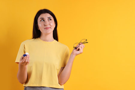 Young woman choosing between glasses and contact lenses on orange background. Space for textの写真素材