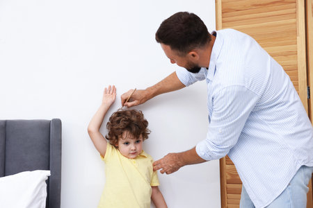 Father measuring her little son's height near white wall at homeの写真素材