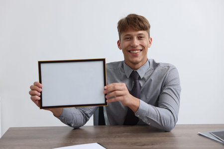 Man with diploma blank frame at desk indoors. Mockup for designの写真素材