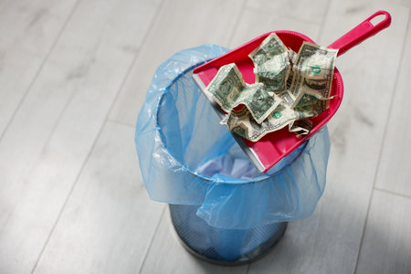 Dollar banknotes, dustpan and trash bin on floor, closeup. Space for textの写真素材