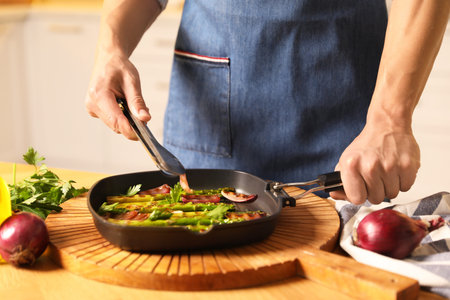 Man adding onion into pan with grilled vegetables at table indoors, closeupの写真素材