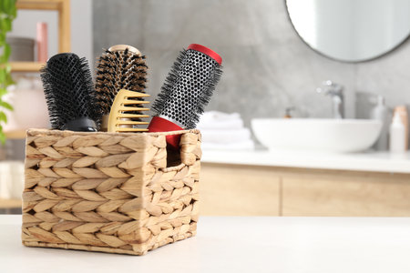 Hair styling. Different combs and brushes in wicker basket on white table in bathroom, closeup. Space for textの写真素材