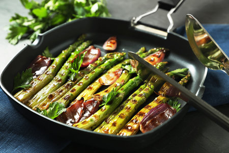 Delicious grilled vegetables with parsley in pan and tongs on table, closeupの写真素材