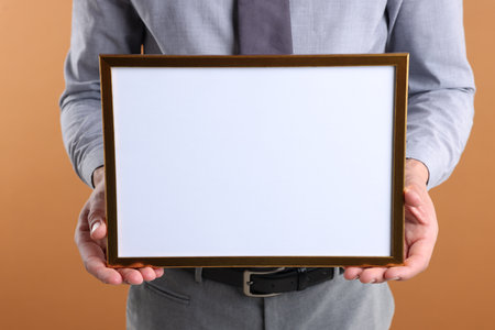 Man with blank frame on pale orange background, closeup. Mockup for designの写真素材