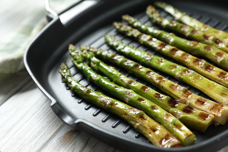 Delicious grilled asparagus in pan on light wooden table, closeupの写真素材