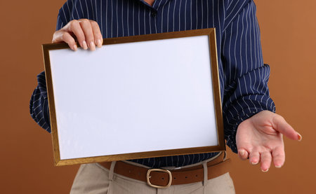Woman with blank frame on brown background, closeup. Mockup for design